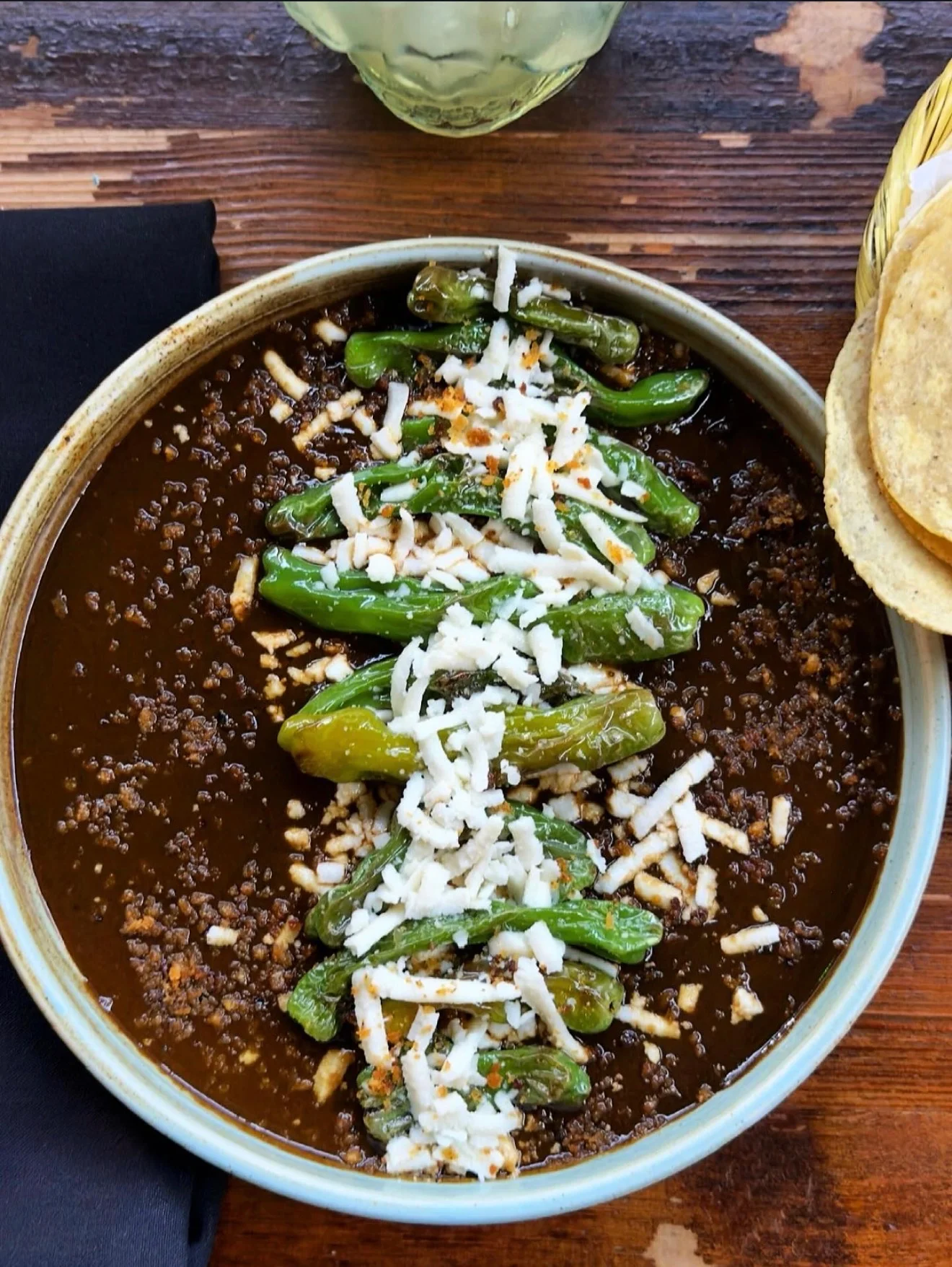 Chilitos toreados topped with crumbled cheese over a dark sauce, with tortillas alongside.