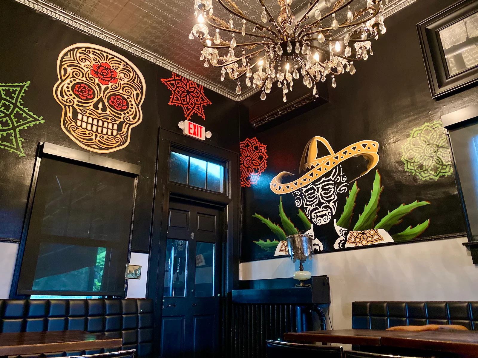 Colorful skull murals, black booth seating, and a crystal chandelier in La Dama’s dining room