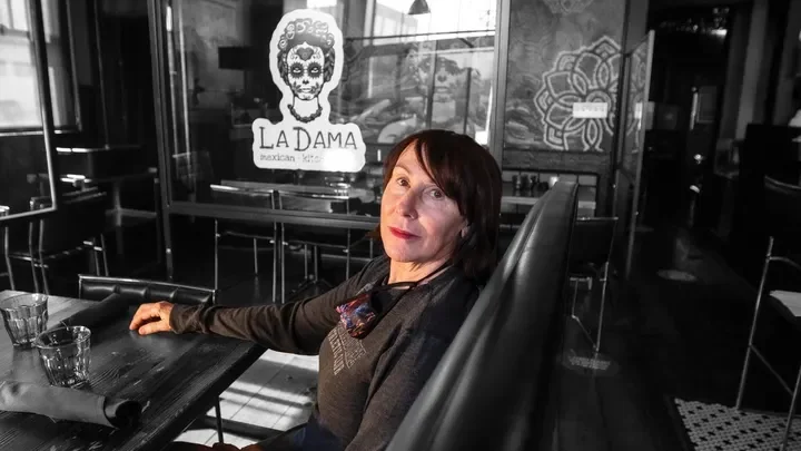 Peggy Magister seated at a table inside La Dama, with the restaurant’s logo behind her