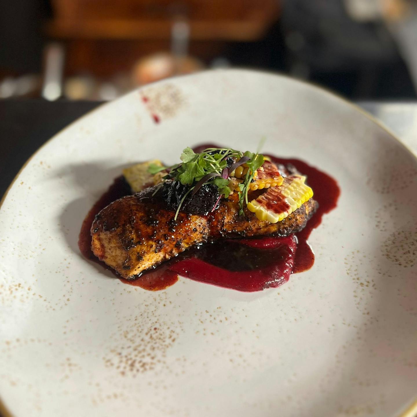 Salmon with corn, greens, and a deep red sauce on a white plate